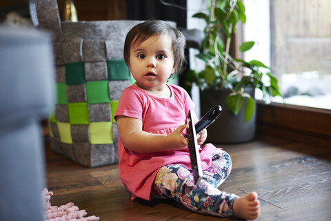 Portrait of cute baby girl sitting on the floor at home holding remote control stock photo