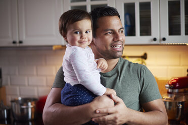 Lächelnder Vater hält kleines Mädchen in der Küche zu Hause - ABIF01115