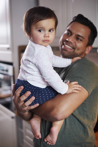 Porträt eines lächelnden Vaters, der ein kleines Mädchen zu Hause hält, lizenzfreies Stockfoto