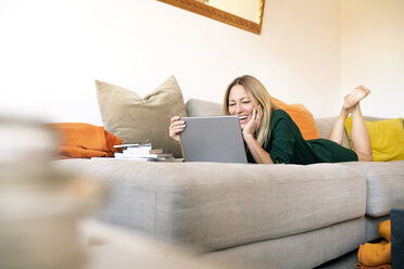Laughing woman relaxing on the couch at home looking at laptop - DMOF00082