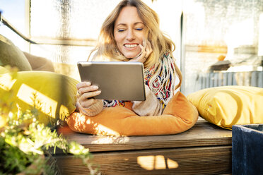 Porträt einer lächelnden blonden reifen Frau, die sich im Wintergarten mit einem digitalen Tablet entspannt - DMOF00094