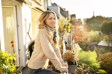 Portrait of smiling blond mature woman standing on balcony at autumn - DMOF00101