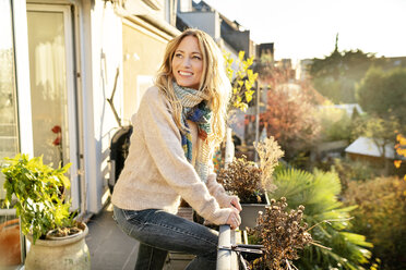 Portrait of smiling blond mature woman standing on balcony at autumn - DMOF00102