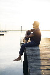 Mann sitzt bei Sonnenuntergang auf einer Mole in Blekinge, Schweden - FOLF09746