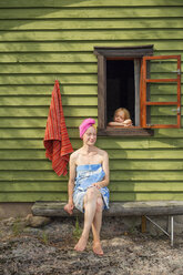 Mittlere erwachsene Frau sitzt vor einer Sauna in Finnland - FOLF09832