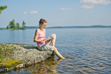 Mittlere erwachsene Frau mit Blick auf ein Tablet vor einem See in Finnland - FOLF09837