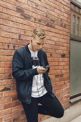Jugendlicher lehnt an einer Mauer und schaut auf sein Handy in Schweden - FOLF09896