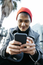 Spanien, Barcelona, Porträt eines lächelnden jungen Mannes, der auf sein Handy schaut - JRFF02492