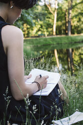 Artist sitting on a meadow near water drawing, partial view - JUBF00317