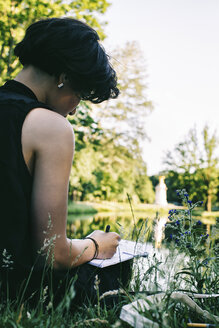 Artist sitting on a meadow near water in a park drawing - JUBF00318