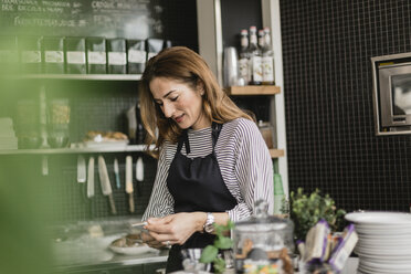 Barista hält Smartphone am Tresen eines Cafés - FOLF10031