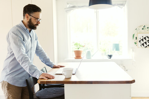 Mittlerer Erwachsener mit Laptop in einem Esszimmer in Schweden, lizenzfreies Stockfoto