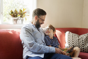 Mid Adult man and boy using a device in a living room in Sweden - FOLF10054