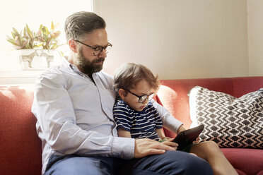 Mid Adult man and boy using a device in a living room in Sweden - FOLF10055