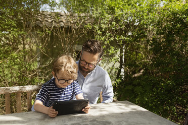 Mid adult man and boy use a device at an outdoor table in Sweden - FOLF10058