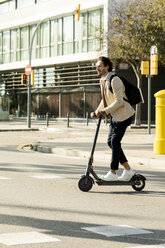 Man with backpack crossing the street on E-Scooter - VABF02061