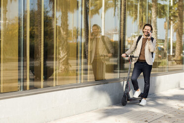 Lachender Mann am Telefon mit E-Scooter in der Stadt - VABF02065