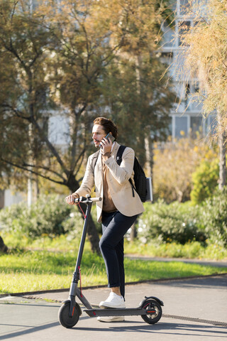 Mann beim Telefonieren mit Rucksack und E-Scooter, lizenzfreies Stockfoto