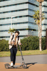 Mann mit Rucksack und E-Scooter schaut auf sein Handy - VABF02072