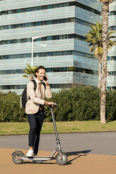 Laughing man on the phone with backpack and E-Scooter in the city - VABF02073