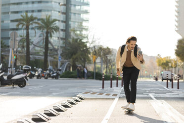 Mann schaut beim Skateboardfahren in der Stadt auf sein Handy - VABF02081