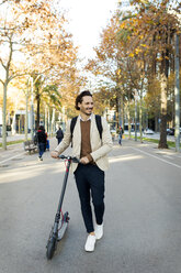 Lächelnder Mann mit Rucksack E-Scooter in der Stadt - VABF02089