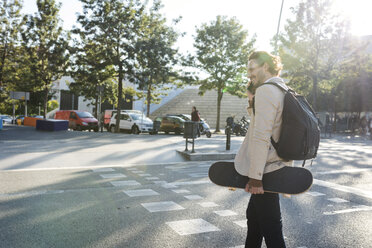 Mann am Telefon mit Rucksack und Skateboard beim Überqueren der Straße - VABF02094