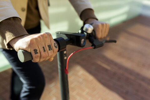 Hand of tattooed man holding handlebar of E-Scooter, close-up stock photo