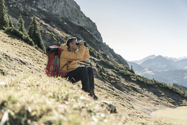 Österreich, Tirol, Mann macht Pause beim Wandern in den Bergen und schaut durch ein Fernglas - UUF16354