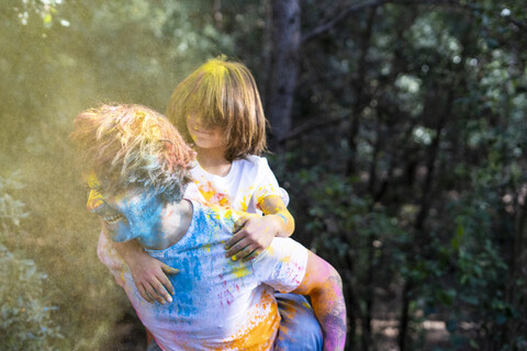 Vater trägt Sohn huckepack, voll mit buntem Farbpulver, beim Feiern von Holi, dem Fest der Farben, lizenzfreies Stockfoto