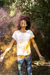 Woman standing in cloud of colorful powder paint, celebtaing Holi festival - ERRF00459