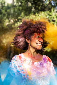 Frau schüttelt den Kopf, voll mit buntem Farbpulver, beim Feiern von Holi, dem Fest der Farben - ERRF00470