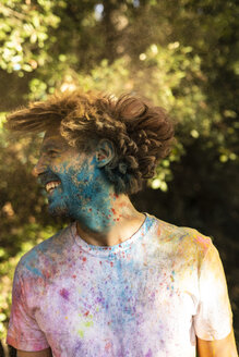 Mann schüttelt den Kopf, voll mit buntem Farbpulver, und feiert Holi, das Fest der Farben - ERRF00476