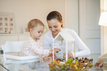 Mutter und kleine Tochter basteln ein herbstlich dekoratives Haus zu Hause - DIGF05572