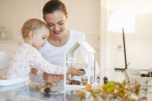 Mutter und kleine Tochter basteln ein herbstlich dekoratives Haus zu Hause - DIGF05576
