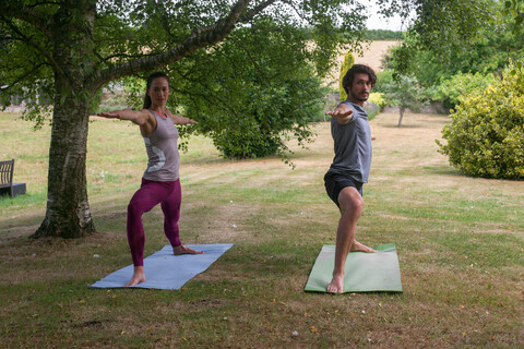 Mann und Frau machen Yoga im Garten, üben Kriegerhaltung, lizenzfreies Stockfoto