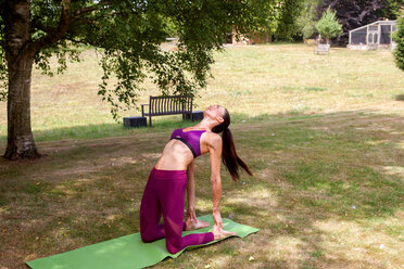 Woman practicing yoga in garden, bending over backwards - CUF46583