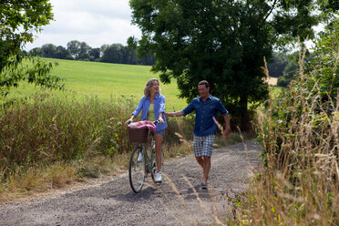 Älteres Paar beim Spazierengehen und Radfahren auf einer Landstraße - CUF46592