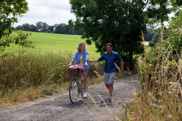 Mature couple strolling and cycling on rural road - CUF46592