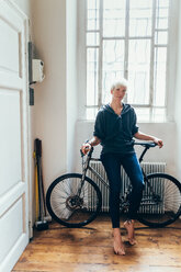 Woman sitting on bicycle at home - CUF46683