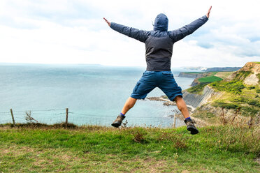 Man jumping on clifftop by sea, Bournemouth, UK - CUF46725