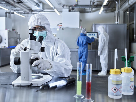 Chemiker, die in einem Industrielabor arbeiten, Schutzkleidung tragen und ein Mikroskop benutzen - CVF01107