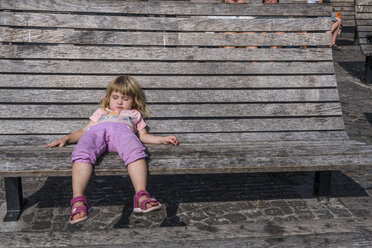 Sweden, girl lying on wooden bench on town square - RUNF00944