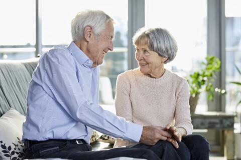 Älteres Paar sitzt auf der Couch und spricht miteinander, lizenzfreies Stockfoto