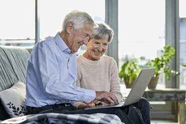 Senior couple sitting together on couch using laptop - RBF07002