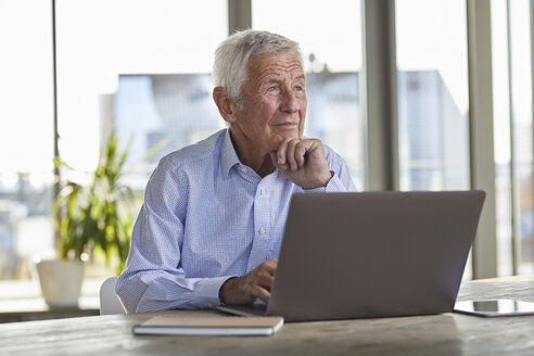 Porträt eines nachdenklichen älteren Mannes, der mit einem Laptop am Tisch sitzt und in die Ferne schaut - RBF07003