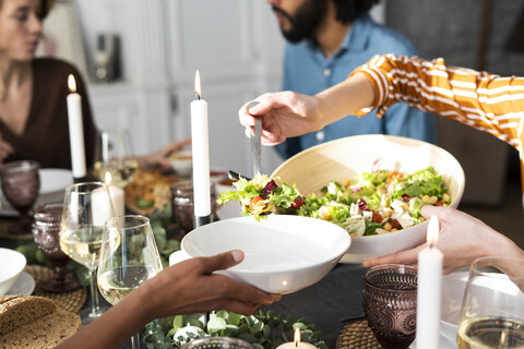 Frau serviert Salat auf dem Teller eines Freundes bei einer Dinnerparty, lizenzfreies Stockfoto