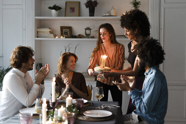Friends surprising young woman with a birthday cake with burning candles - ERRF00594