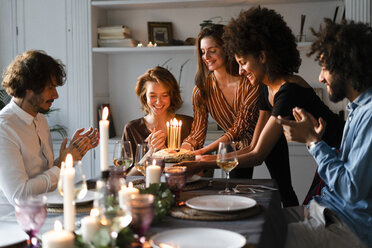 Friends surprising young woman with a birthday cake with burning candles - ERRF00595