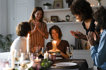 Friends surprising young woman with a birthday cake with burning candles - ERRF00596